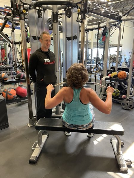 Trainer Joe coaching an older client on a seated cable row.